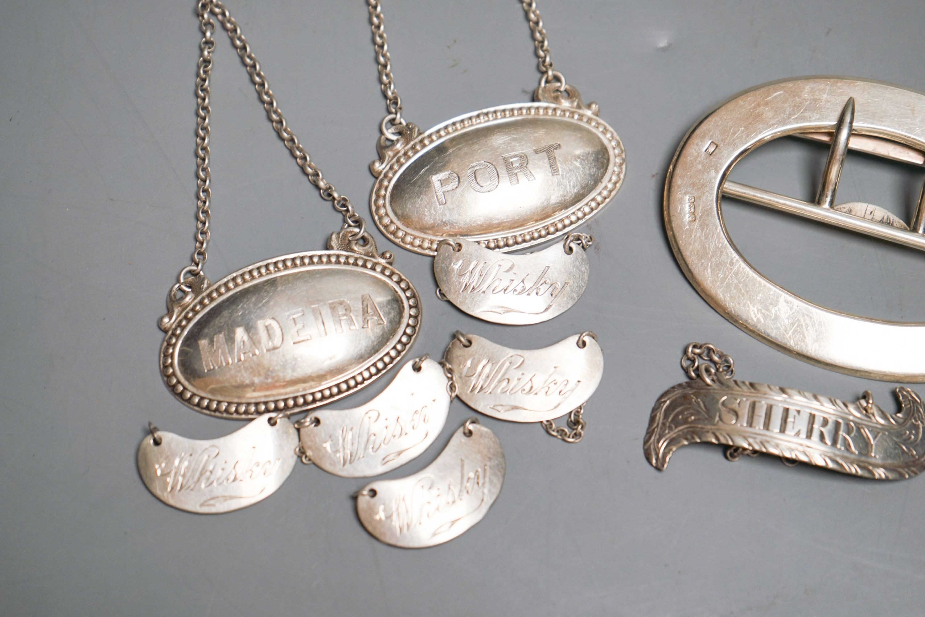 Eight assorted mainly 20th century silver wine labels and a n Edwardian silver belt buckle, 98 grams.